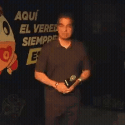 Man Holding Microphone In Front Of Sign Aqui El Ver Siempre GIF