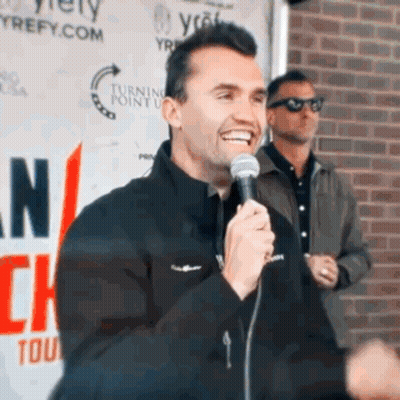 Man Holding Microphone Smiling In Front Of Turning Point Sign GIF