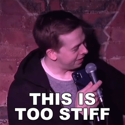 Man Holding Microphone With This Is Too Stiff Behind Him GIF