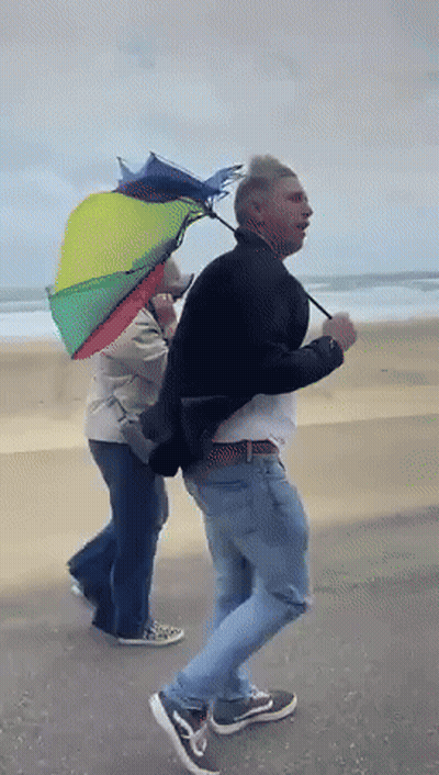 Man Holding Rainbow Umbrella Walking On Beach GIF
