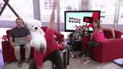 Man Holding Teddy Bear In Front Of TV Saying What's Trending GIF
