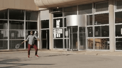 Man Holding Tennis Racquet In Front Of Building With A Sign GIF