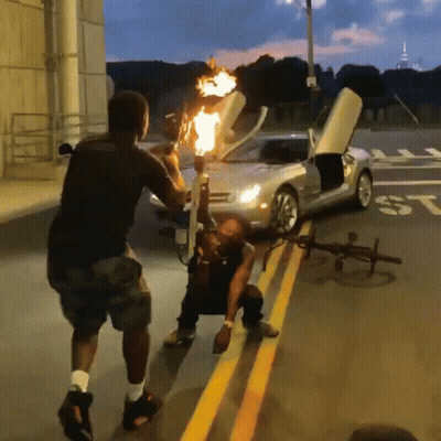 Man Holding Torch In Front Of Car With ST On Side GIF