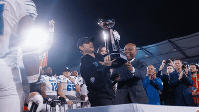 Man Holding Trophy In Front Of Denver Football Players GIF