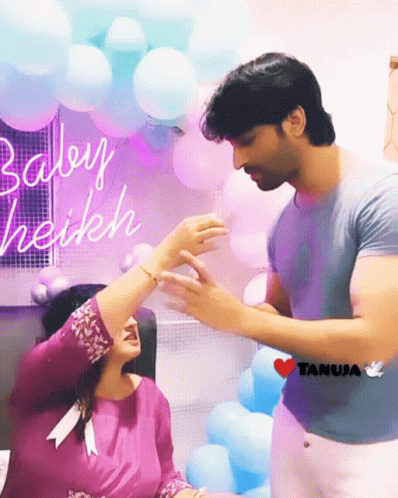 Man Holding Woman's Hand In Front Of Balloons And Baby Haikeh Sign GIF