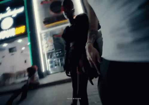 Man Holding Woman's Hand In Front Of Wild Bitches Store GIF