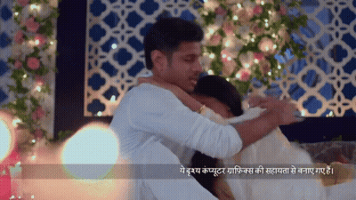 Man Hugging Woman In Front Of Flower Wall With Lights GIF