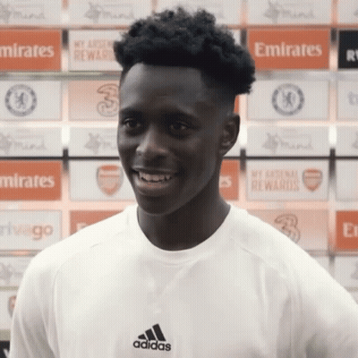 Man In Adidas Shirt Smiling In Front Of Emirates Ads GIF