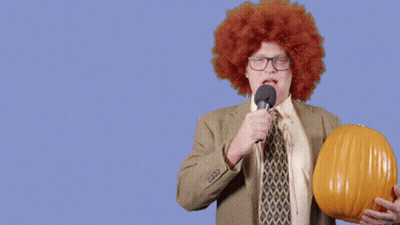 Man in Afro Wig Holding Pumpkin and Microphone Says Happy Halloween