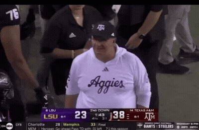 Man In Aggies Shirt In Front Of Scoreboard During Football Game GIF