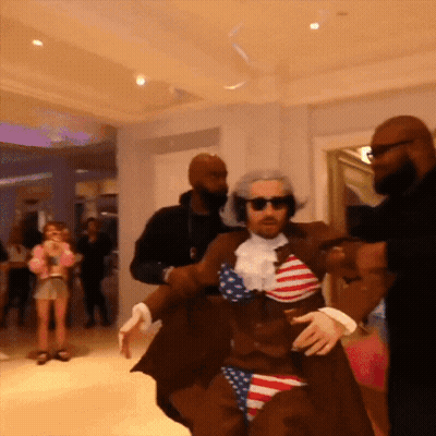 Man In American Flag Costume Escorted By Two Men GIF