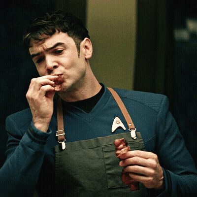 Man In Apron And Star Trek Badge Eating Meat GIF