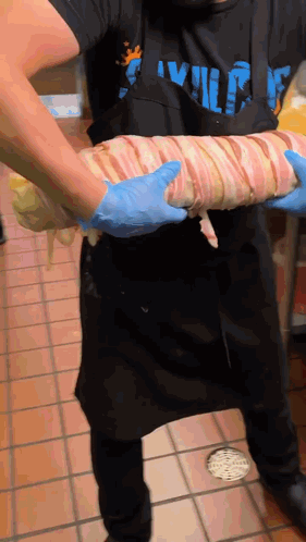 Man In Apron Holding Bacon Wrapped Meat GIF