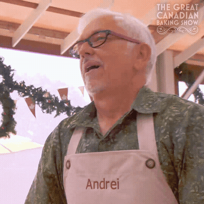 Man In Apron Saying Andrei In Front Of The Great Canadian Baking Show Sign GIF