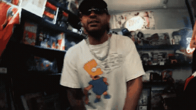 Man In Bart Simpson Shirt With Toy Shelf GIF