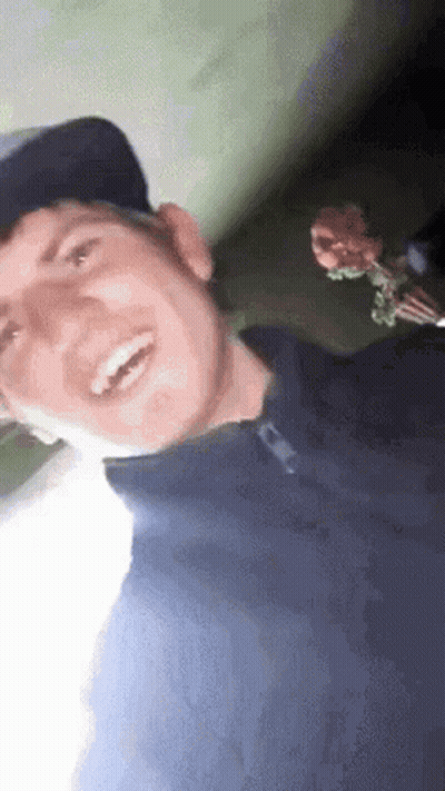 Man In Baseball Cap Blue Shirt Smiling Holding Flower GIF