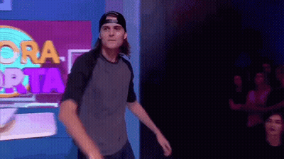 Man In Baseball Cap Dancing In Front Of Ora Prata Sign GIF