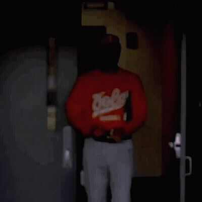 Man In Baseball Jersey And Sunglasses Walking Through Dark Room GIF