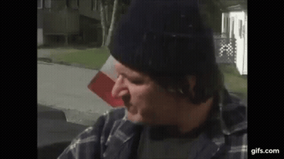 Man In Beanie And Plaid Shirt Sitting In Front Of Flag GIF