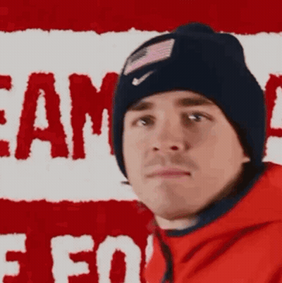Man In Beanie And Red Jacket In Front Of Flag GIF