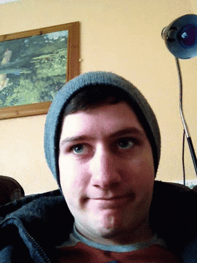 Man In Beanie Looks At Camera With Lamp Behind Him GIF