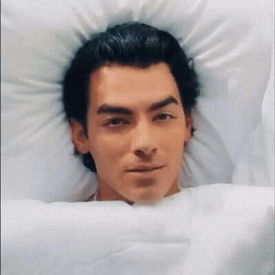 Man In Bed Head On Pillow Looking At Camera GIF