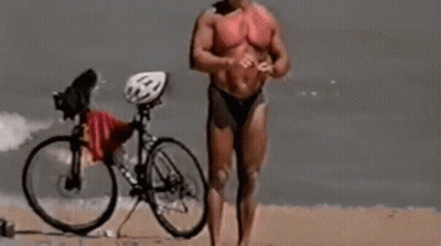 Man In Bikini Standing On Beach With Bike GIF