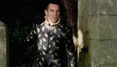 Man In Black And Gold Suit Standing Before Stone Wall GIF