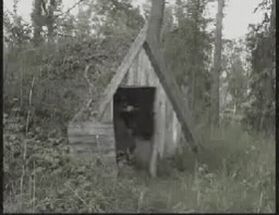 Man In Black And White Photo Holding Gun In Front Of Wooden Building GIF