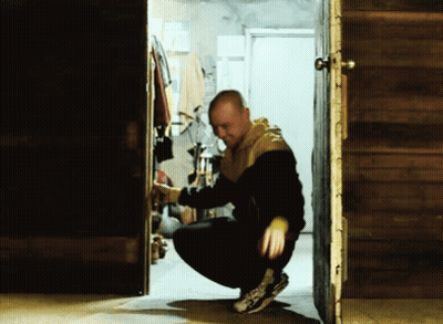 Man In Black And Yellow Jacket Squatting In Doorway GIF