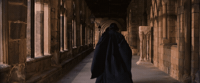 Man In Black Cloak Walking Stone Hallway GIF