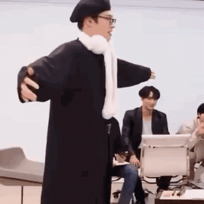 Man In Black Coat And White Scarf Standing In Front Of Group GIF