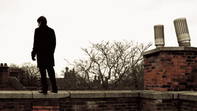 Man In Black Coat Standing On Brick Wall GIF