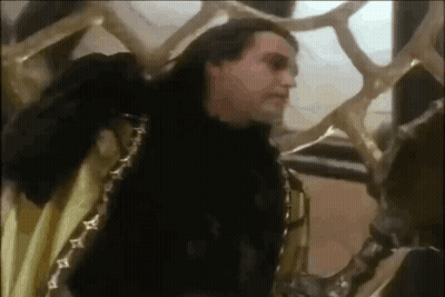 Man In Black Fur Coat Standing Next To Snake Statue GIF