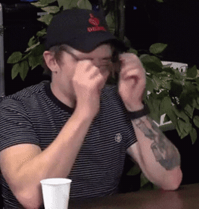 Man In Black Hat With Apple Sitting At Table With Cup GIF