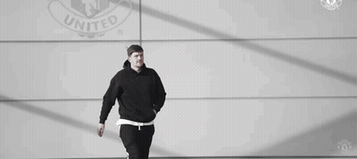 Man In Black Hoodie And Pants Walking In Front Of United Logo Wall GIF