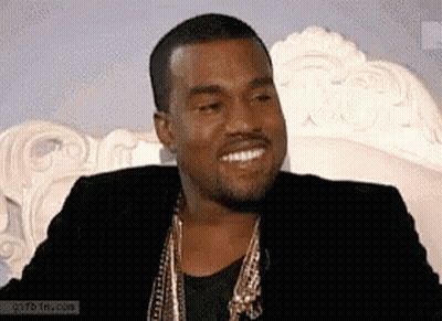 Man In Black Jacket And Gold Chains Smiling On Couch GIF