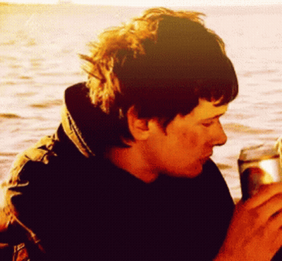 Man In Black Jacket Drinking From Can In Front Of Ocean GIF