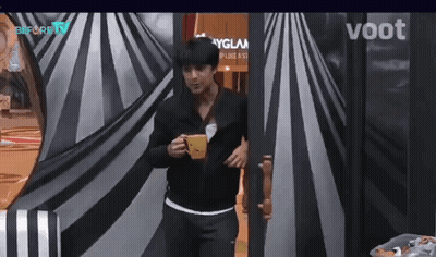 Man in Black Jacket Holding Coffee in Front of Voot Sign