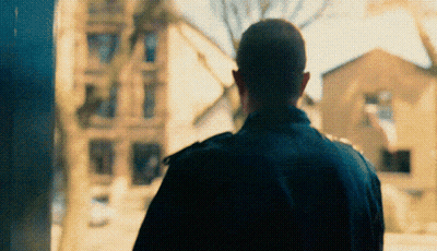 Man In Black Jacket In Front Of Blurry Building GIF