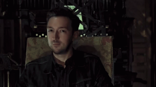 Man In Black Jacket Sitting In Chair Looking At Camera GIF