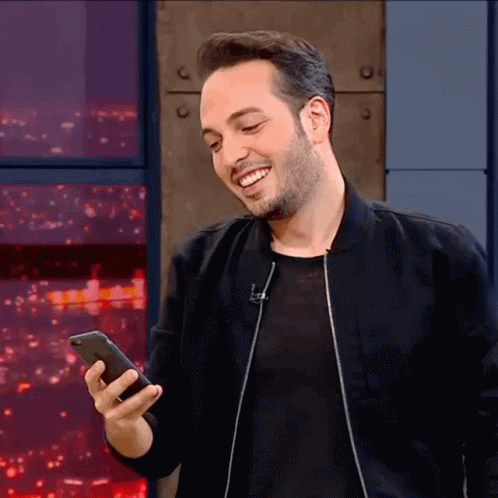 Man In Black Jacket Smiling Holding Phone GIF