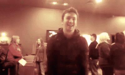 Man In Black Jacket Smiling In Crowded Room GIF