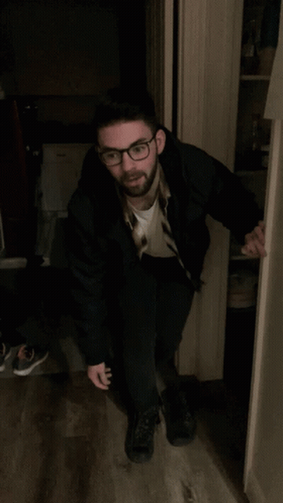 Man In Black Jacket Standing In Doorway With Arms Up GIF