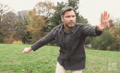 Man In Black Jacket With SNL Logo In Grassy Field GIF