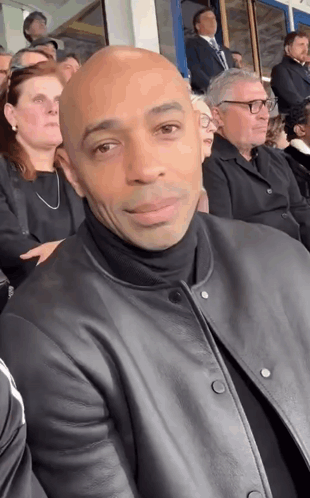 Man In Black Leather Jacket Sitting In Crowd GIF