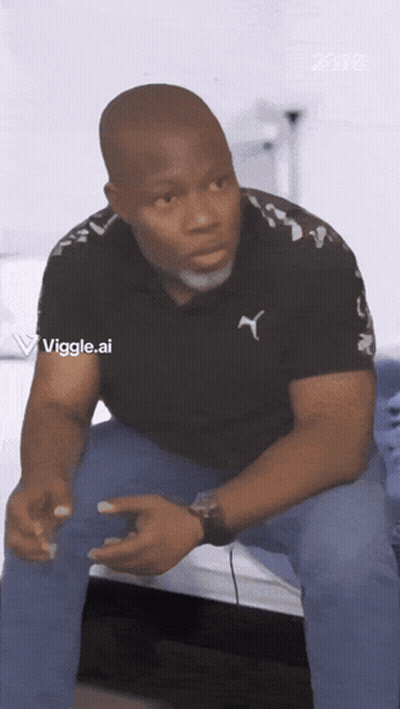 Man In Black Puma Logo Shirt Sitting On Bed GIF