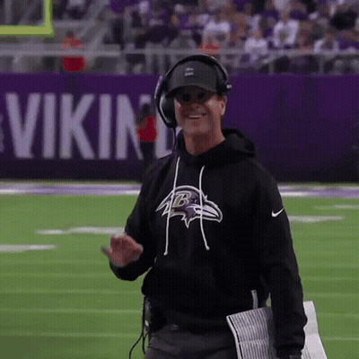 Man In Black Ravens Sweatshirt And Headphones Walking On Football Field GIF