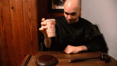Man In Black Robe Sitting With Cup GIF