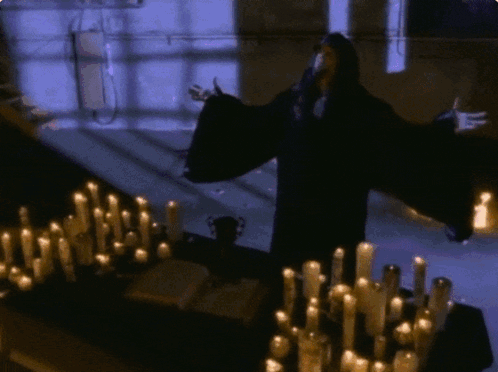 Man In Black Robe Standing Before Candles GIF